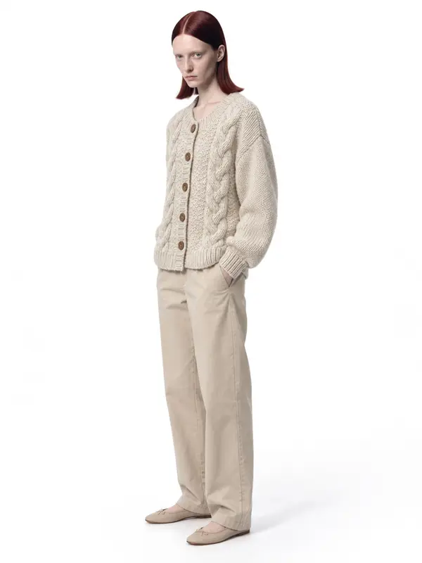 Cream cable-knit cardigan on an AI model, white wall, three-quarter