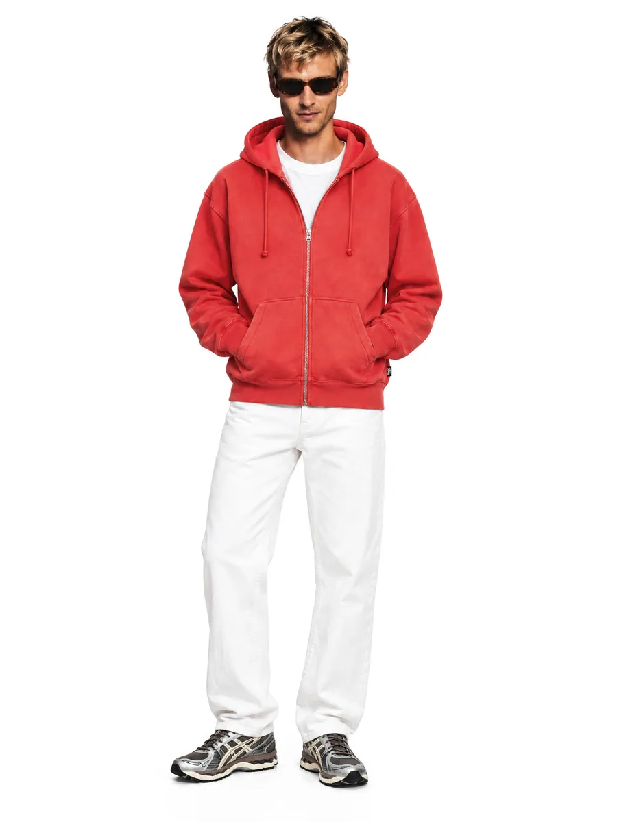 Red Stüssy hoodie on a model, hands in pockets